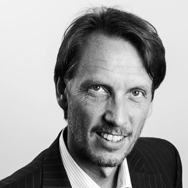 Black-and-white headshot of a smiling man in a pinstripe suit against a neutral background. (Informative headshot)