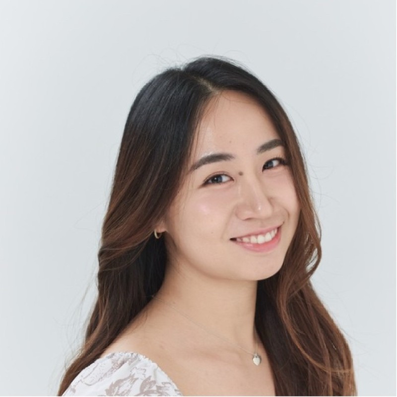Smiling young Asian woman with long dark hair, wearing a light lace top and a small heart pendant necklace.